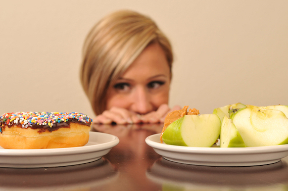 girl looking at a plate of donuts and a plate of apples