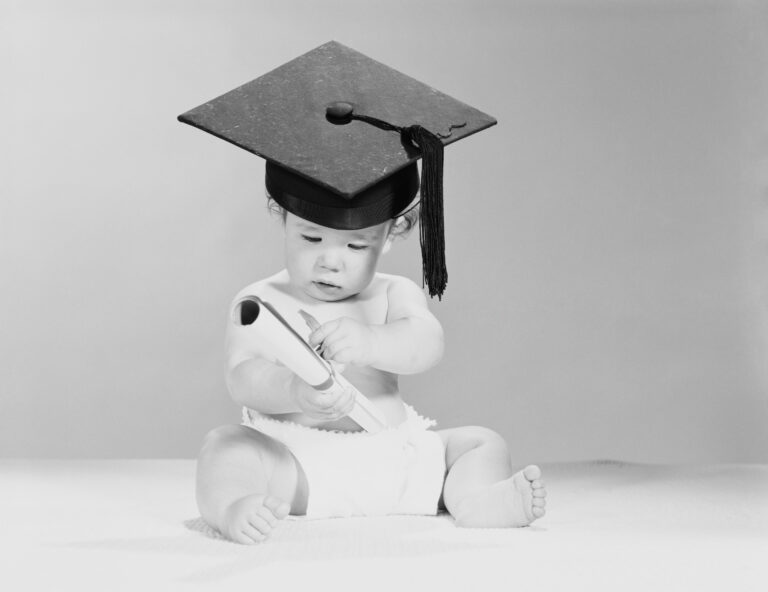 Baby in diaper, holding diploma and wearing graduation cap.